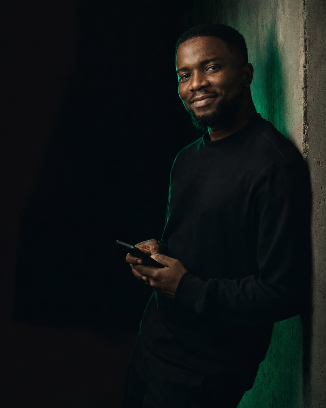 Founder leaning on a concrete wall with a phone, lit by a green rim light