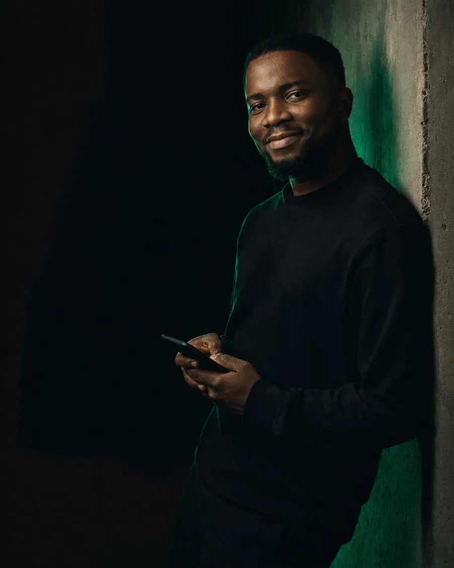 Founder leaning on a concrete wall with a phone, lit by a green rim light